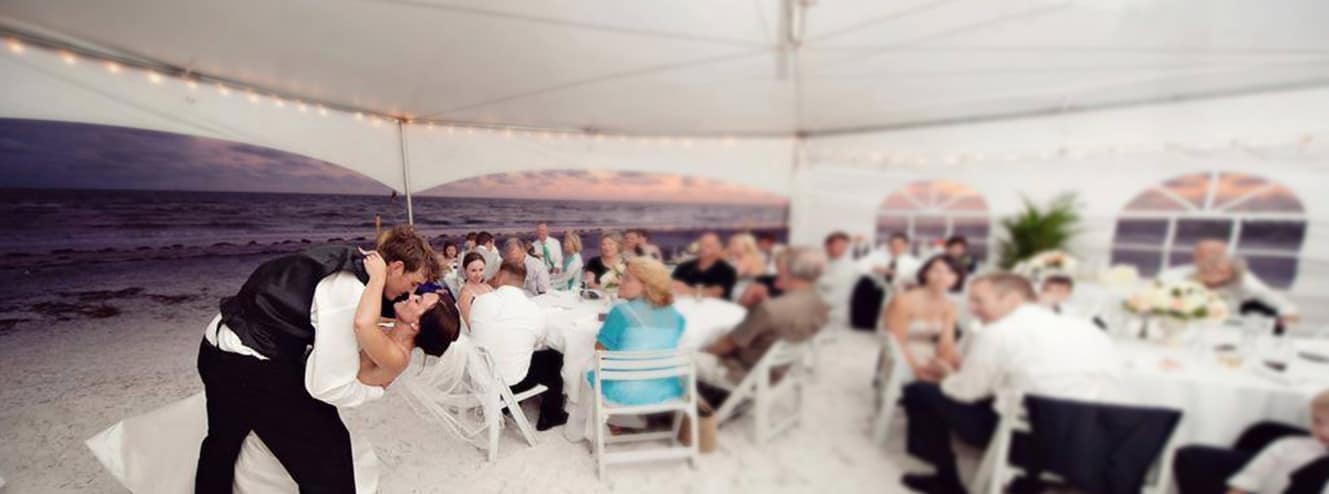 Groom dipping Bride at beach side tent wedding reception